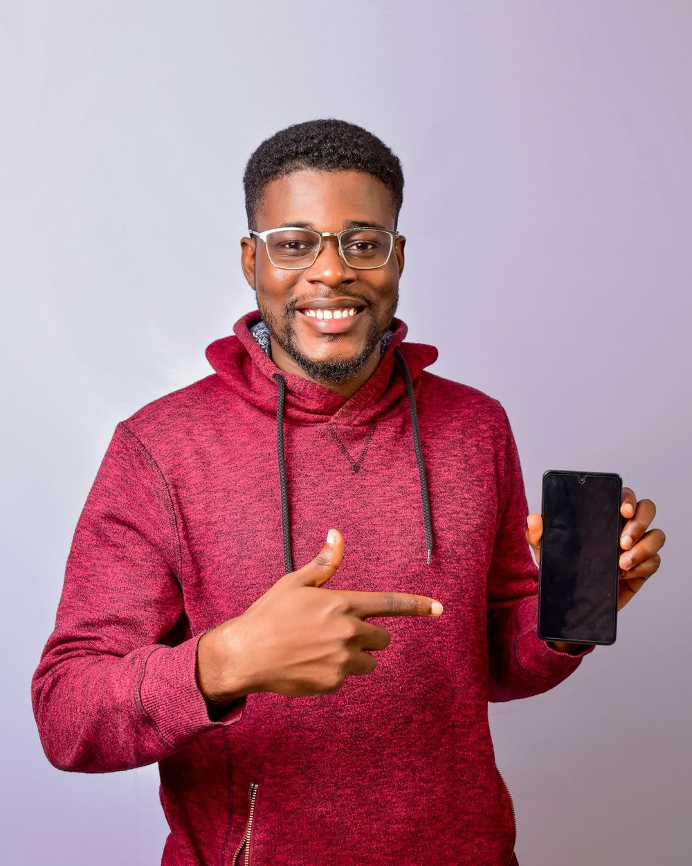 A man in a red hoodie smiling and pointing at the phone in his hand.